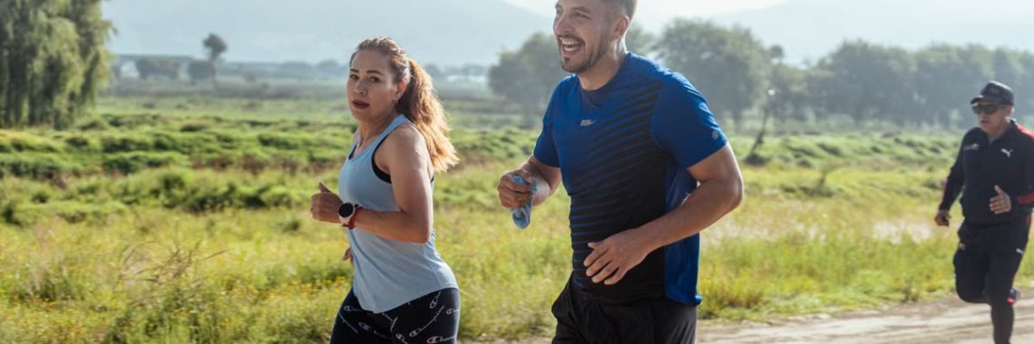 Two adults running on a rural dirt path, enjoying a sunny day outdoors.